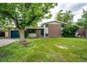 This house features a charming exterior with a brick facade, lawn, mature trees, and attached garage at 3111 Troy St, Aurora, CO 80011