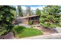 A mid-century modern home with brick and wood accents surrounded by mature trees and manicured landscaping at 6975 S Chase Ct, Littleton, CO 80128