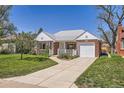 Traditional brick home with manicured lawn, mature trees, and a driveway leading to a garage at 5703 Ammons St, Arvada, CO 80002