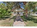 Charming white two-story home with front porch and walkway to the front door surrounded by mature trees at 7801 Valley View St, Louviers, CO 80131