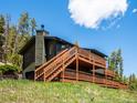 Side view of a home with a large deck and stairs, siding, chimney, and a yard on a sunny day at 34075 Grouse Ln, Evergreen, CO 80439