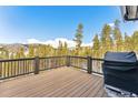 Wooden deck with black railings overlooking trees and mountains, featuring a grill at 1279 Estates Dr, Breckenridge, CO 80424