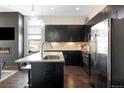 Open kitchen with black cabinetry, stainless appliances, island with seating, and fireplace in living area at 336 E 1St Ave # 209, Denver, CO 80203
