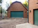 View of a detached garage with wood siding, a large green door, and exterior sconces at 9274 Sandy Ln, Conifer, CO 80433