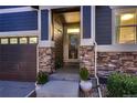 Close-up of the home's entrance highlighting stone pillars, a glass storm door, and decorative potted plants at 25 N Irvington St, Aurora, CO 80018