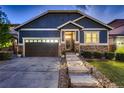 Attractive home showcasing stone veneer, blue siding, well-lit walkway, and a two-car garage at 25 N Irvington St, Aurora, CO 80018