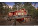 Red two-story home with large wooden deck, stairs, and an under-deck patio area with blue chairs at 6997 S Columbine Rd, Evergreen, CO 80439