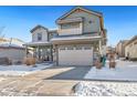 Two-story house with gray exterior, stone accents, and three-car garage, snow on ground at 16382 Spanish Peak Way, Broomfield, CO 80023