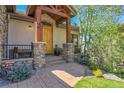 Inviting front porch featuring stone columns, a wooden door, and manicured landscaping at 1007 Nob Hill Rd, Evergreen, CO 80439
