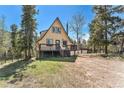 A-frame cabin with a deck surrounded by lush greenery and tall trees, set against a clear blue sky at 9185 Jill Dr, Conifer, CO 80433