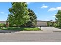 The exterior of the one-story home boasts a two-car garage, concrete driveway, and mature shade trees on the lawn at 5030 Titan Ct, Denver, CO 80239