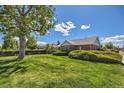 Brick home with manicured green lawn and mature trees, complemented by a bright blue sky with clouds at 2361 Olive St, Denver, CO 80207