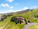 Aerial view of luxury home with mountains, trees, and sprawling lawns under blue skies at 6634 Window Rock Ln, Morrison, CO 80465
