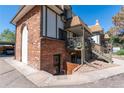 Side view of a brick townhouse with a stairwell entrance, a car port, and a small decorative fire pit at 2700 S Holly St # 115, Denver, CO 80222