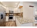 Bright kitchen with stainless steel appliances, granite countertops, white cabinets, and wooden floors at 6105 Verbena Ct # 103, Erie, CO 80516