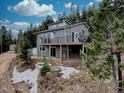 Two-story gray home nestled on a hillside with mature trees and a deck overlooking the natural landscape at 31932 Steven Way, Conifer, CO 80433