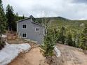 Gray two-story home with snow still on the ground surrounded by the mountain forest on a cloudy day at 31932 Steven Way, Conifer, CO 80433