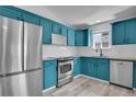 Corner view of the kitchen showing modern blue cabinets and stainless steel appliances with tile backsplash at 3470 W Walsh Pl, Denver, CO 80219