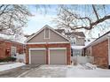 Two-car garage with brick and siding exterior, snow-covered driveway at 9875 Greensview Cir, Lone Tree, CO 80124