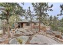 View of a house nestled among mature trees and large rock formations on a hillside at 27857 Apex Cir, Evergreen, CO 80439