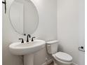 White powder room with a pedestal sink, round mirror, and elongated toilet at 574 Penn Rd, Elizabeth, CO 80107