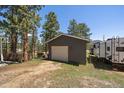 Exterior view of a detached one-car garage with white door and gray siding next to a camper at 29827 Gigi Rd, Evergreen, CO 80439