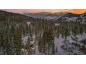 Aerial view shows snow-covered mountains, evergreens, and stone home, creating a serene and picturesque setting at 2383 Tiger Rd, Breckenridge, CO 80424