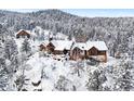 Snowy exterior shot of the sprawling log home on a rocky ridge, accented by snow-covered forest and a small log cabin at 8699 Blue Creek Rd, Evergreen, CO 80439