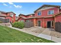 Red townhome exterior featuring a well-maintained lawn and landscaped pathway at 1775 Aspen Meadows Cir, Denver, CO 80260
