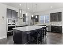 A spacious kitchen with dark cabinets, a mosaic backsplash, stainless steel appliances, and a large center island at 1867 W 137Th Ln, Broomfield, CO 80023