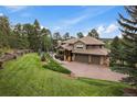 Expansive lawn with mature trees frames this house with an attached garage and stone-and-wood accents at 1456 Shavano Ct, Evergreen, CO 80439