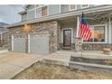 Close up of home exterior with stone accents, attached two-car garage, and covered front porch. American flag shown at 1793 E 164Th Pl, Brighton, CO 80602