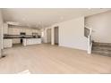 Open-concept living space with hardwood floors seamlessly connecting the living room, kitchen, and staircase at 718 N Clubview St, Watkins, CO 80137