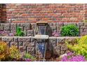Close-up of a brick water feature with cascading water, colorful plants, and lush greenery at 11771 Elk Head Range Rd, Littleton, CO 80127