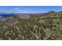 Aerial view of a house nestled amongst green trees and mountains with snow-capped peaks in the distance at 3945 Douglas Mountain Dr, Golden, CO 80403