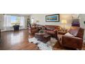 Cozy living room featuring hardwood floors, leather furniture, and a large window with natural light at 2190 Coyote Creek Dr, Fort Lupton, CO 80621