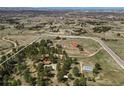A high angle aerial showcases the property with horse facilities, buildings, and a home nestled among trees and open land at 7076 Inspiration Dr, Parker, CO 80138