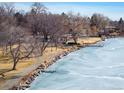 Picturesque lake view with frozen water, stone embankment, walkway, bare trees, and blue skies at 4470 W Lakeridge Rd, Denver, CO 80219