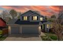 Charming two-story home featuring a gray exterior, brick accents, an attached two car garage, and a vibrant sunset at 2314 Flagstaff Dr, Longmont, CO 80504