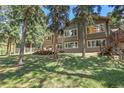 Expansive backyard with a wooden deck, surrounded by mature trees and lush greenery at 7753 Red Fox Dr, Evergreen, CO 80439