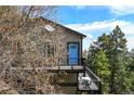 Gray two-story home with a blue door and black metal balcony, surrounded by trees at 8386 S Davco Dr, Morrison, CO 80465