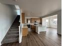 Open-concept kitchen boasts an island with a sink, hardwood floors, wooden cabinets, and seamlessly connects to the staircase at 7243 Prairie Sage Ln, Littleton, CO 80125