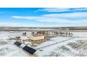 Expansive rural property featuring a ranch-style home, a large barn, solar panels, and a fenced yard in a snowy landscape at 4075 Merada Ct, Franktown, CO 80116