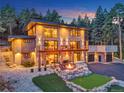 Striking multi-story home boasts a well-lit stone facade, balcony, fire pit, and putting green against a backdrop of lush trees at 7793 Elk Path Way, Morrison, CO 80465