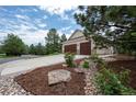 Three-car garage with wooden doors and a well-maintained yard featuring mulch and rock landscaping at 1030 Timbercrest Dr, Castle Pines, CO 80108