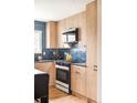 Close up of kitchen featuring light wood cabinets, blue tile backsplash, and stainless steel appliances at 815 S Jersey St, Denver, CO 80224