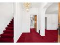 Bright hallway featuring staircase, chandelier, fresh white walls, and bright red carpeting at 2146 Federal Blvd, Denver, CO 80211