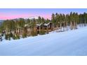 Exterior view of a log home nestled among pine trees, adjacent to a snowy ski slope, with a backdrop of mountains at 422 Timber Trail Rd, Breckenridge, CO 80424