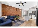 Inviting living area with exposed brick wall, hardwood floors, and cozy blue couch with open concept to the kitchen at 2508 Kensing Ct, Denver, CO 80211