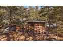 Cozy log cabin featuring a stone chimney, American flag, and plentiful firewood storage at 121 Mary Beth Rd, Evergreen, CO 80439